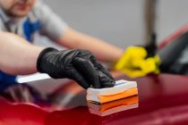 Man worker of car detailing studio applying ceramic coating on car paint with sponge applicator.