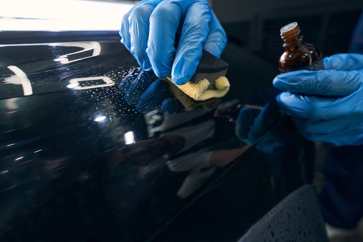 Automotive technician using microfiber applicator for spreading of ceramic coating on car panel
