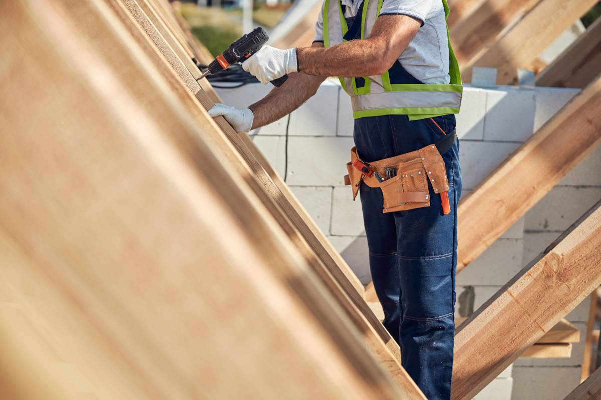 Cropped photo of a construction site worker wearing a handy tool-belt and drilling in the wooden roof frame